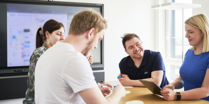 four people stand around a table in a confernce room 